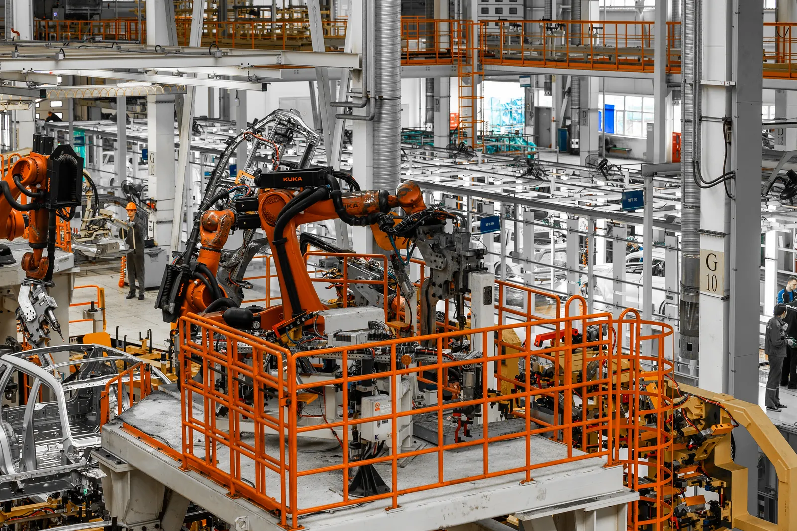 Hala z pomarańczowymi robotami przemysłowymi przy linii montażowej samochodów