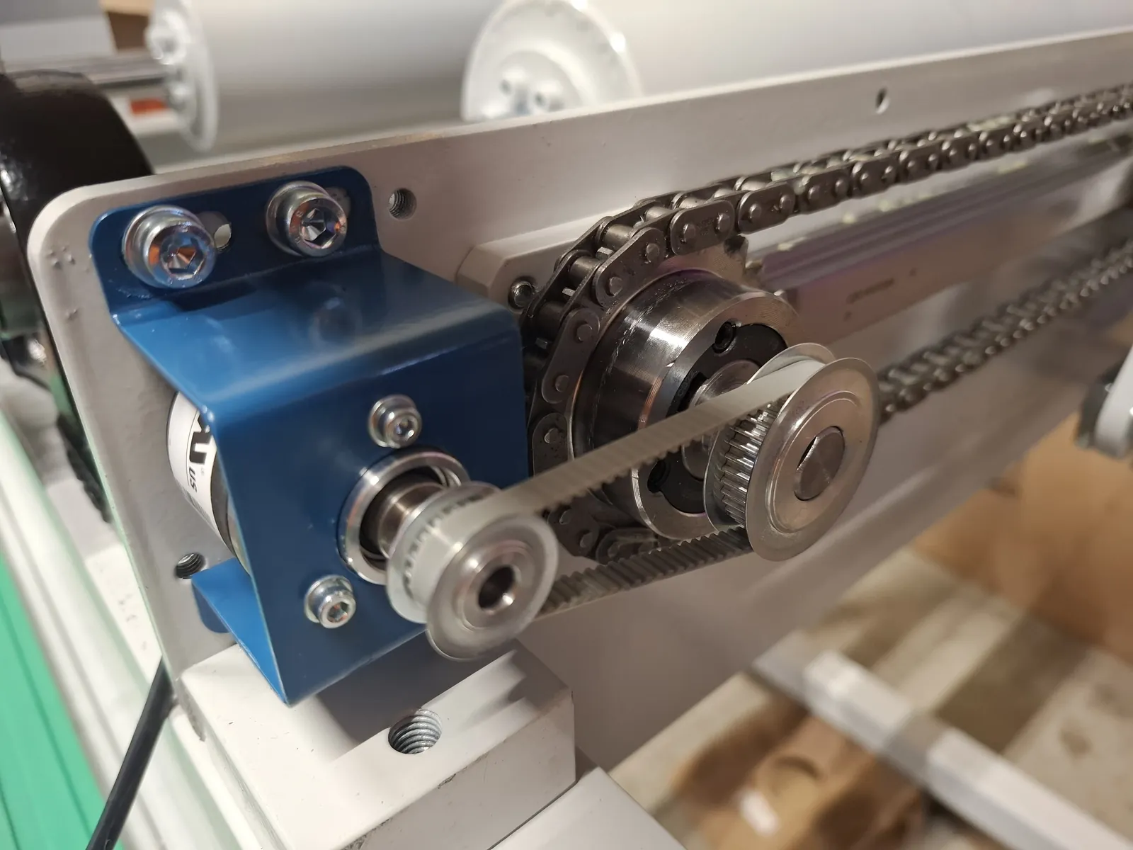 Close-up of a drive with a timing pulley and a chain by a blue bracket