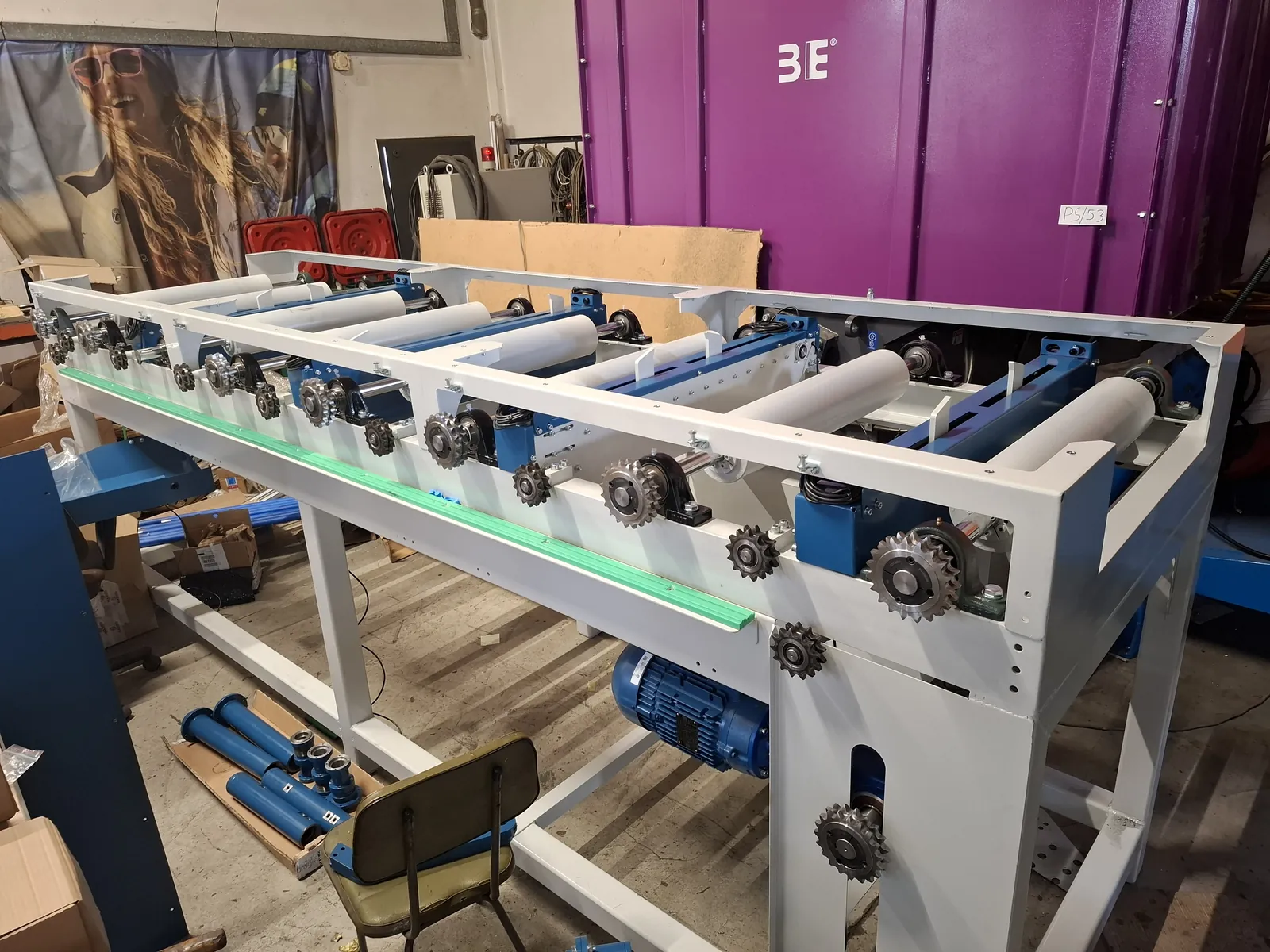 White frame with rollers, sprockets and a motor in a workshop