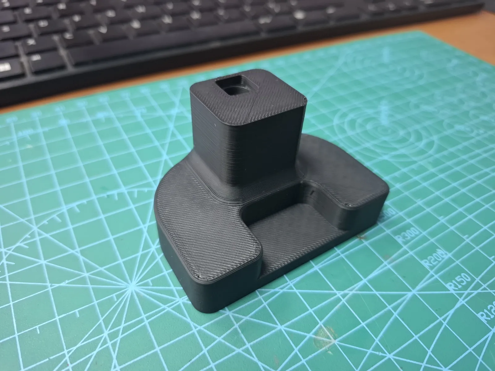 Black 3D-printed part with a square socket on a cutting mat