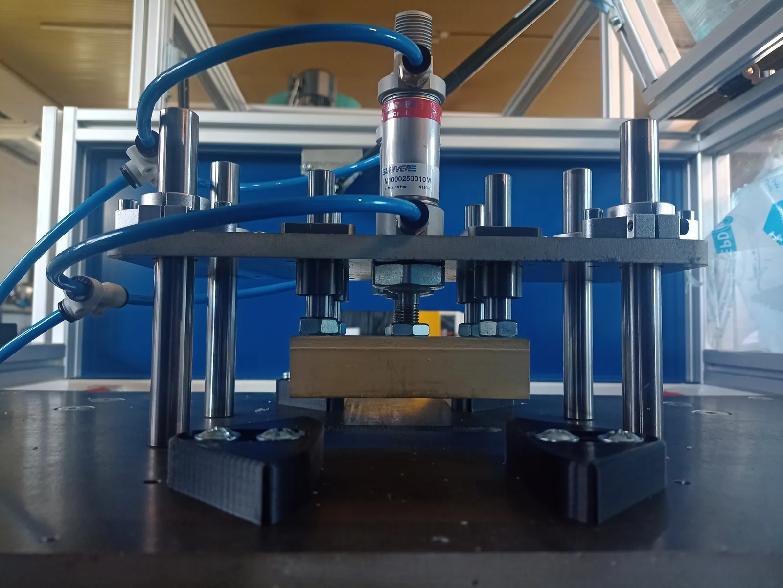 Assembly with a sensor, guides and blue pneumatic hoses above a plate
